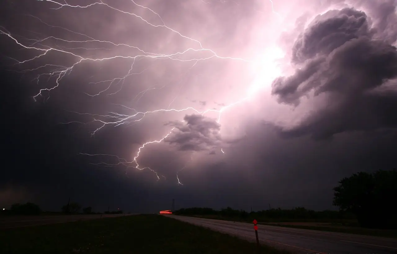 Several lightning bolts striking under a dark purple storm sky beside a road